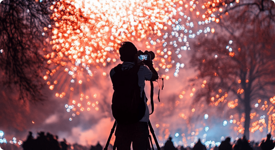 カメラを構え花火を撮影するシルエットと夜空に広がる花火